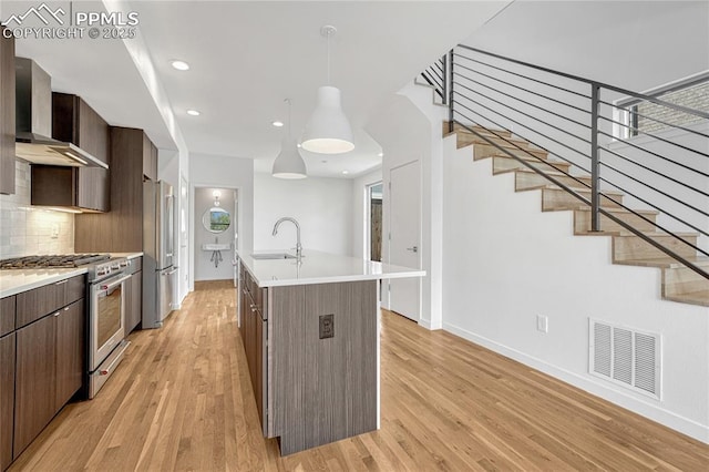 1231 Newton St, Denver, CO 80204 - kitchen featuring wall chimney exhaust hood, appliances with stainless steel finishes, light wood-style flooring, tasteful backsplash, and dark brown cabinets