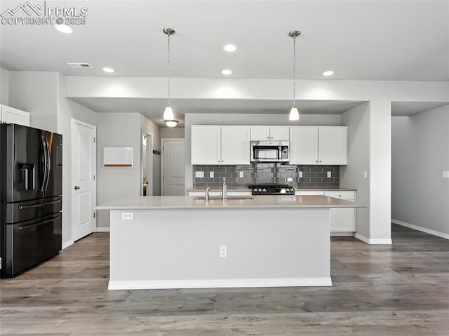 6222 Barr Pt, Colorado Springs, CO 80924 - kitchen featuring black fridge with ice dispenser, stainless steel microwave, decorative backsplash, white cabinetry, and a center island with sink