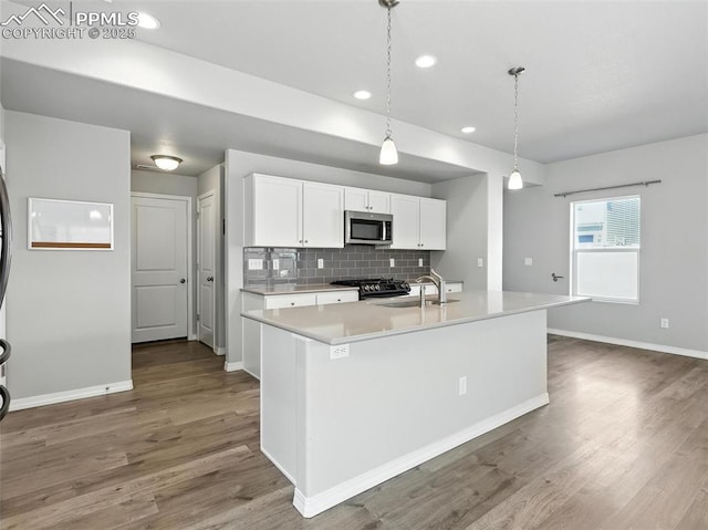 6222 Barr Pt, Colorado Springs, CO 80924 - kitchen with stainless steel microwave, gas stove, white cabinets, wood finished floors, and light countertops