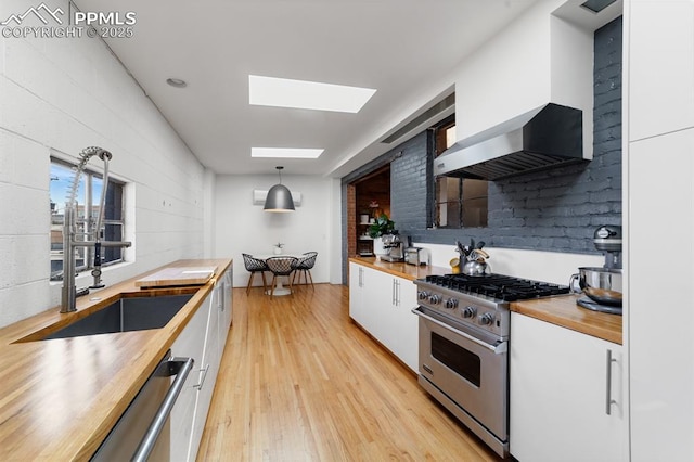 423 W 4th St, Pueblo, CO 81003 - kitchen featuring butcher block countertops, appliances with stainless steel finishes, wall chimney range hood, white cabinets, and a skylight