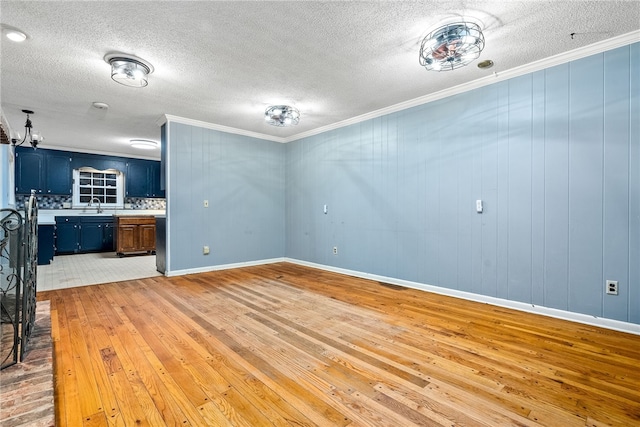 unfurnished living room with light wood-type flooring, sink, crown molding, and wooden walls