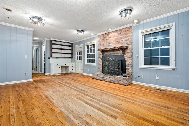 unfurnished living room featuring light wood-type flooring, a textured ceiling, crown molding, and a fireplace