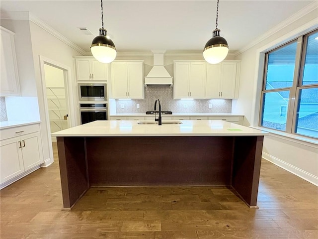 kitchen featuring appliances with stainless steel finishes, custom exhaust hood, tasteful backsplash, a center island with sink, and crown molding