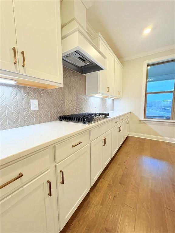 kitchen featuring premium range hood, light wood-type flooring, backsplash, stainless steel gas stovetop, and white cabinets