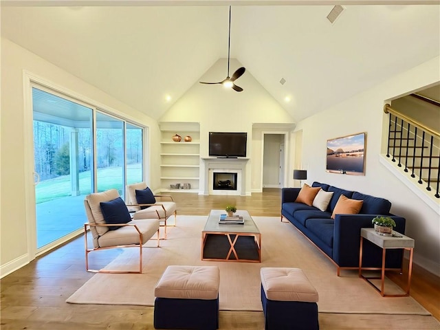 living room featuring built in shelves, stairway, a fireplace, and wood finished floors