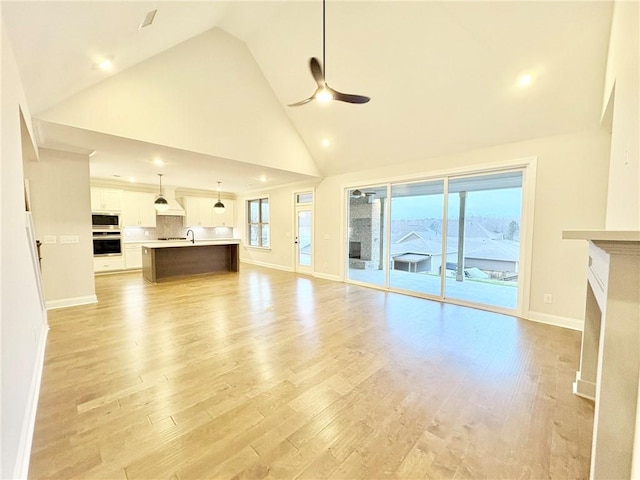 unfurnished living room with ceiling fan, sink, high vaulted ceiling, and light wood-type flooring