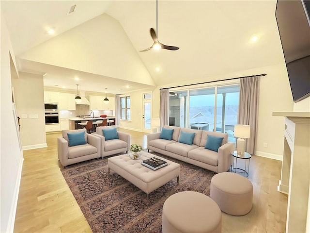 living area featuring high vaulted ceiling, a fireplace, a ceiling fan, baseboards, and light wood-type flooring