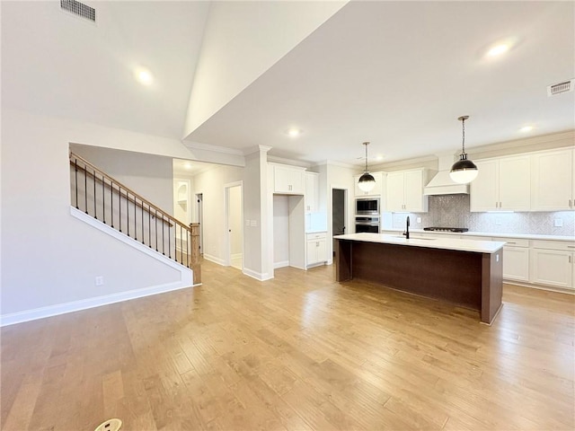 kitchen with white cabinetry, an island with sink, built in microwave, decorative backsplash, and stainless steel oven