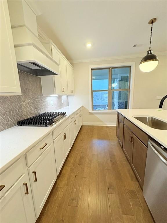 kitchen featuring pendant lighting, sink, white cabinets, stainless steel appliances, and light hardwood / wood-style flooring