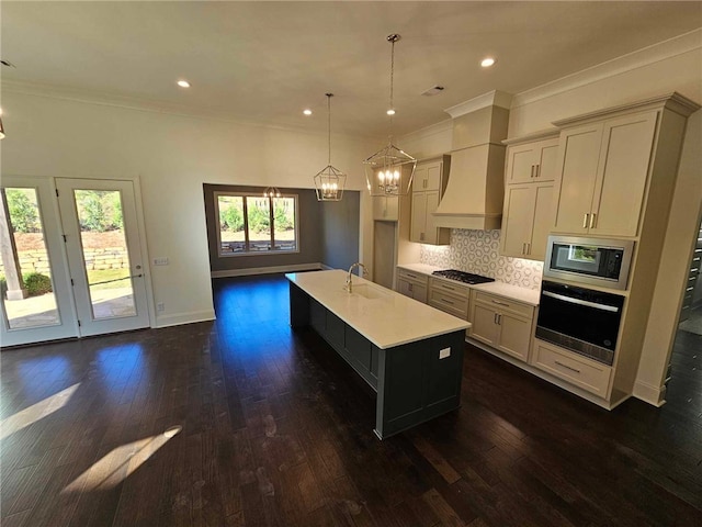 kitchen with backsplash, premium range hood, hanging light fixtures, an island with sink, and appliances with stainless steel finishes