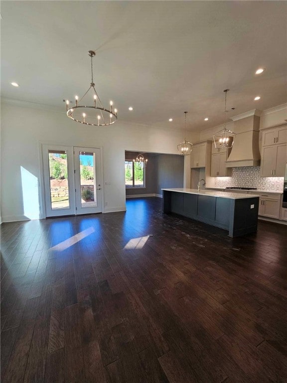 kitchen featuring backsplash, a kitchen island with sink, dark hardwood / wood-style floors, decorative light fixtures, and custom range hood