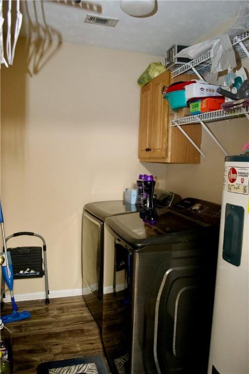 washroom featuring dark wood-style flooring, visible vents, washer and dryer, water heater, and cabinet space