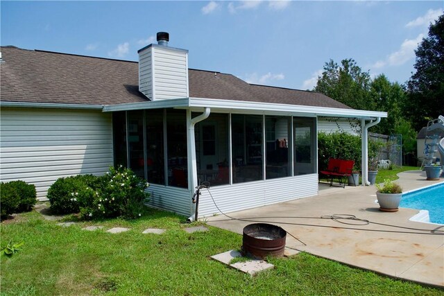 back of property featuring a sunroom, a yard, a chimney, and a patio