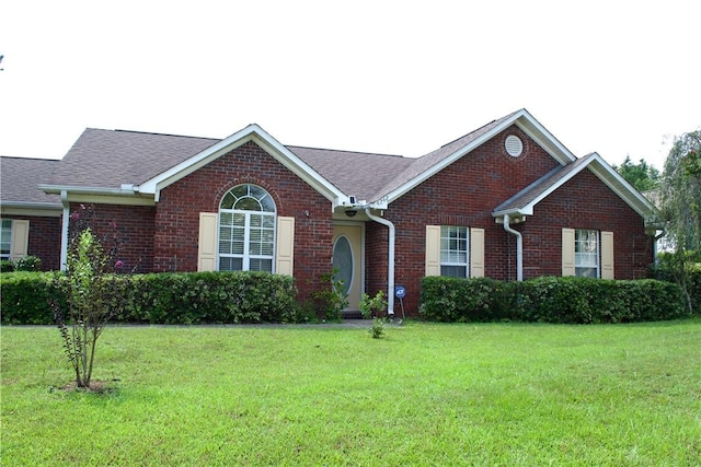 single story home featuring brick siding, roof with shingles, and a front yard