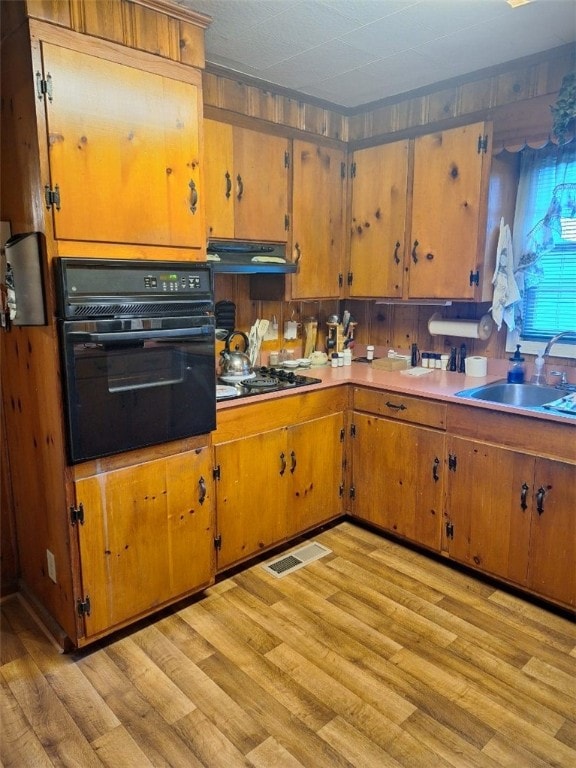 1701 53rd St, Valley, AL 36854 - kitchen featuring black oven, cooktop, under cabinet range hood, light wood-type flooring, and brown cabinetry