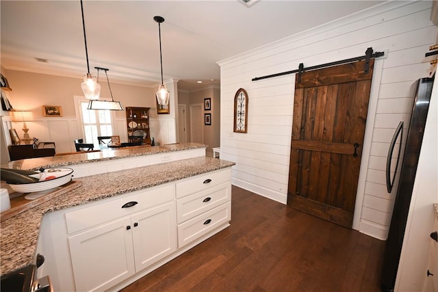 kitchen with light stone counters, pendant lighting, black refrigerator, and white cabinets