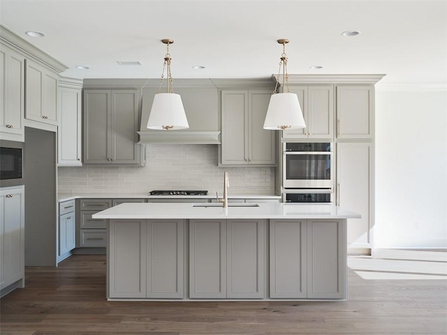 kitchen with hanging light fixtures, sink, gray cabinetry, gas stovetop, and a center island with sink