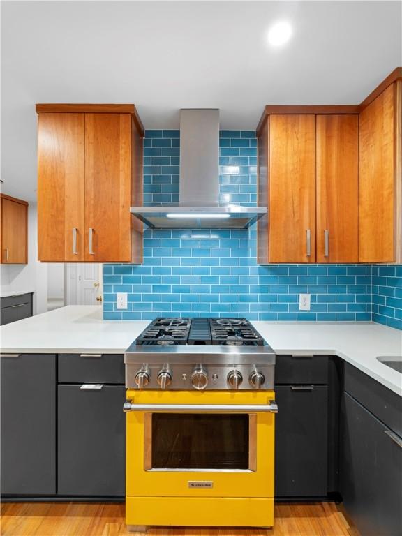 kitchen featuring light hardwood / wood-style floors, wall chimney range hood, backsplash, and stainless steel stove