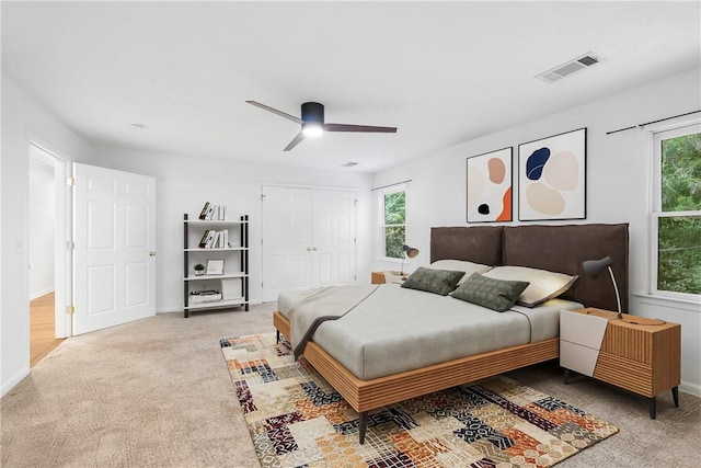 bedroom with ceiling fan, light colored carpet, and a closet