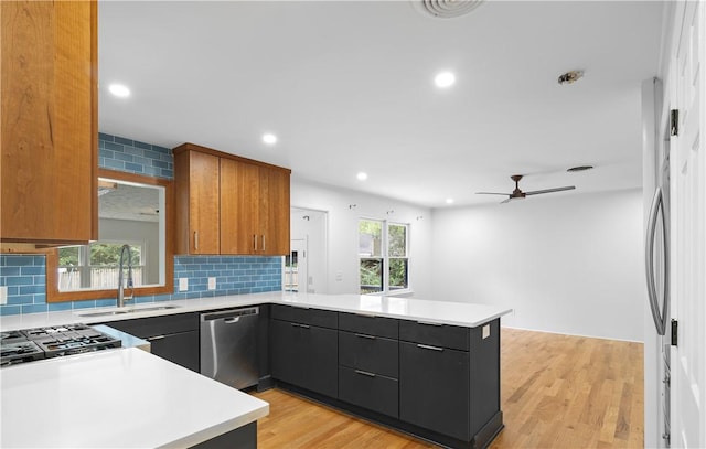 kitchen featuring ceiling fan, dishwasher, sink, kitchen peninsula, and light wood-type flooring