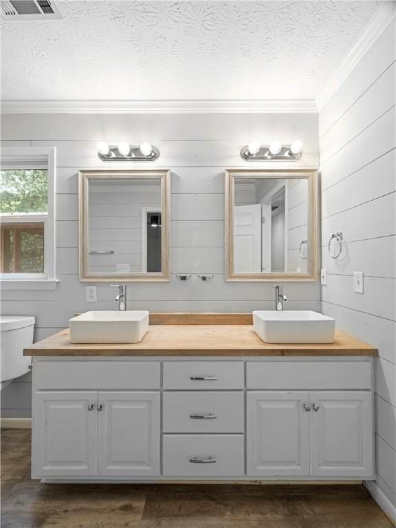 bathroom featuring wood walls, vanity, ornamental molding, and toilet