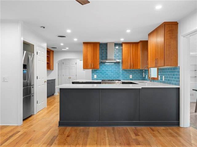 kitchen featuring sink, wall chimney exhaust hood, stainless steel fridge, light hardwood / wood-style floors, and kitchen peninsula