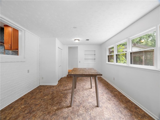 interior space featuring built in features, a textured ceiling, and brick wall