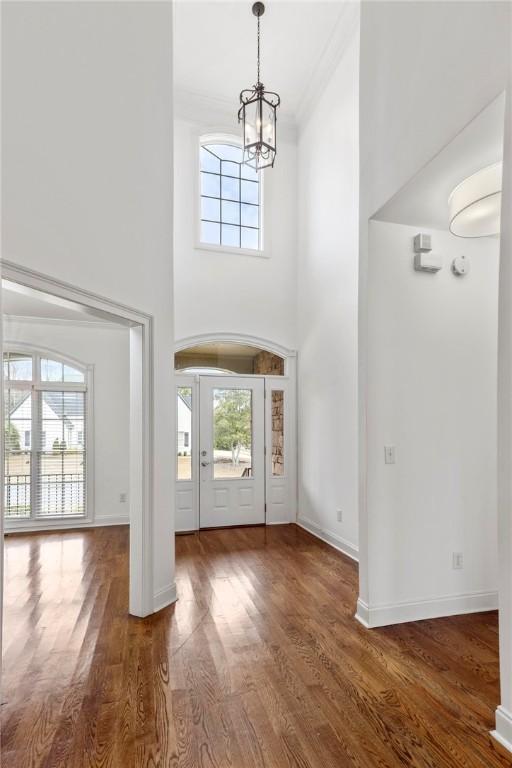 foyer entrance with baseboards, a towering ceiling, wood finished floors, crown molding, and a notable chandelier