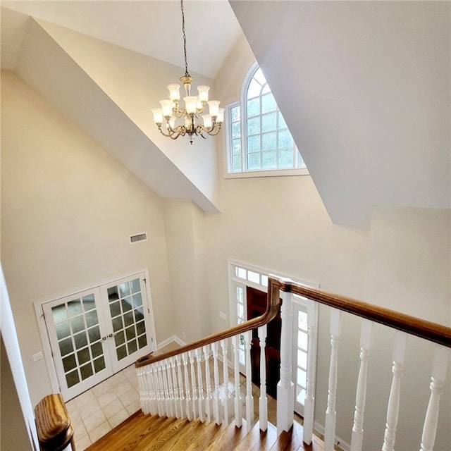 stairway with hardwood / wood-style floors, french doors, high vaulted ceiling, and a chandelier