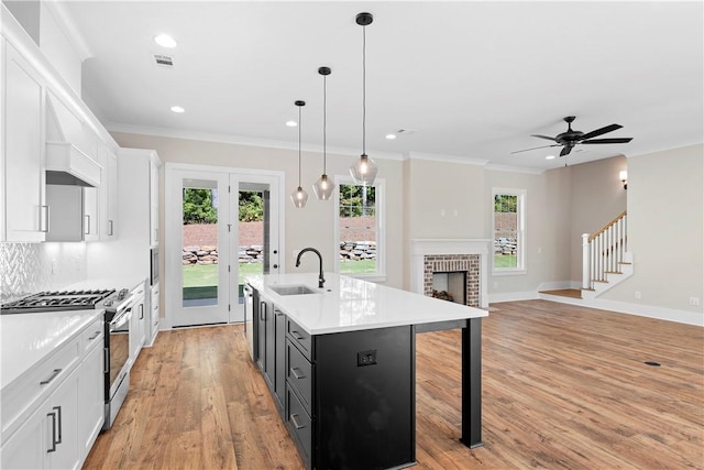 kitchen featuring a center island with sink, decorative light fixtures, gas stove, and white cabinets