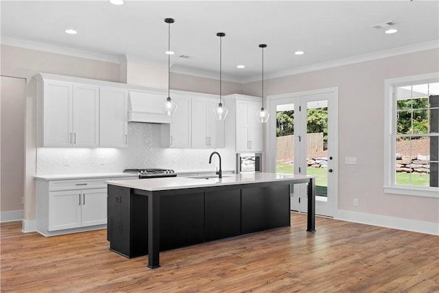 kitchen with a kitchen island with sink, sink, hanging light fixtures, light hardwood / wood-style flooring, and white cabinetry