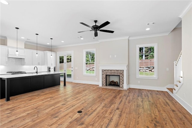 kitchen with light wood-type flooring, ceiling fan, pendant lighting, white cabinetry, and an island with sink