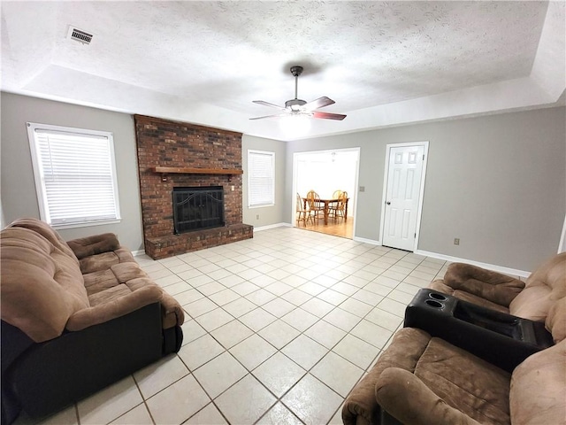 living room featuring a fireplace, a tray ceiling, ceiling fan, a textured ceiling, and light tile patterned flooring