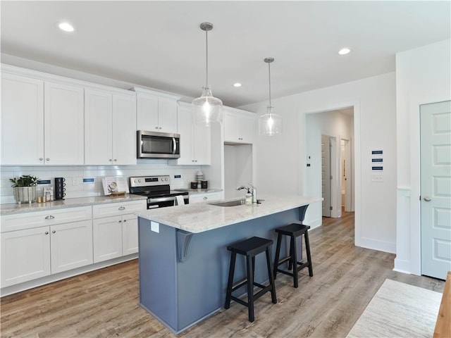 kitchen with appliances with stainless steel finishes, a kitchen island with sink, tasteful backsplash, white cabinets, and decorative light fixtures