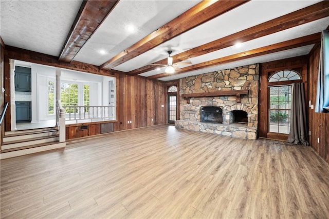 2 Lakewood Cir, Phenix City, AL 36867 - unfurnished living room featuring wooden walls, beamed ceiling, wood finished floors, a stone fireplace, and a ceiling fan