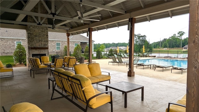 view of patio / terrace with fence, an outdoor living space with a fireplace, a ceiling fan, and a community pool