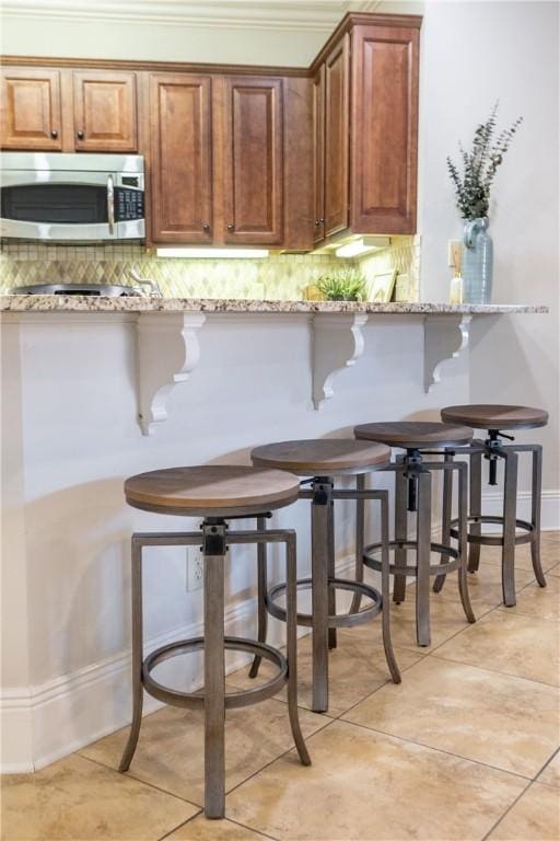 kitchen with a kitchen breakfast bar, kitchen peninsula, light stone countertops, and light tile patterned floors