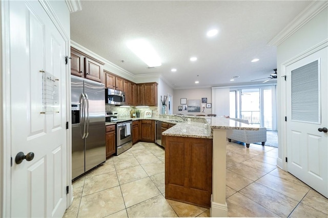 kitchen featuring sink, ornamental molding, light stone counters, kitchen peninsula, and stainless steel appliances