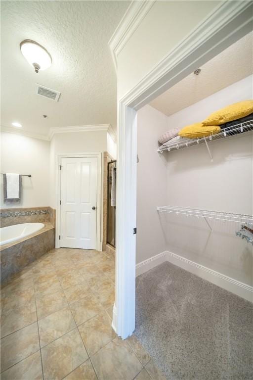 bathroom with tile patterned flooring, a relaxing tiled tub, crown molding, and a textured ceiling