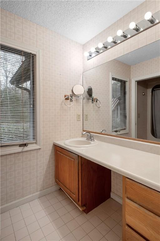 bathroom with a textured ceiling, tile patterned flooring, vanity, and baseboards