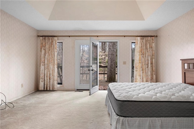 carpeted bedroom with wallpapered walls, access to exterior, and a raised ceiling