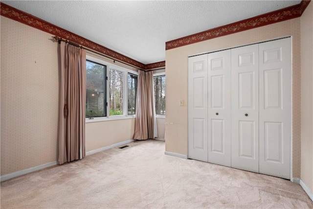 unfurnished bedroom with light carpet, wallpapered walls, baseboards, a textured ceiling, and a closet