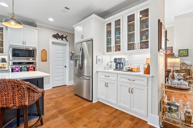 kitchen with white cabinetry, hanging light fixtures, appliances with stainless steel finishes, and light hardwood / wood-style flooring