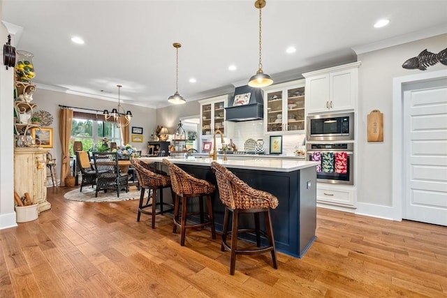 kitchen with premium range hood, a center island with sink, hanging light fixtures, white cabinetry, and stainless steel appliances