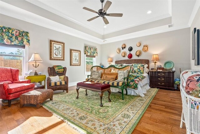 bedroom with ceiling fan, multiple windows, and a tray ceiling