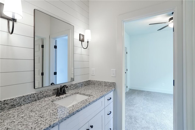 bathroom with wooden walls, baseboards, a ceiling fan, and vanity