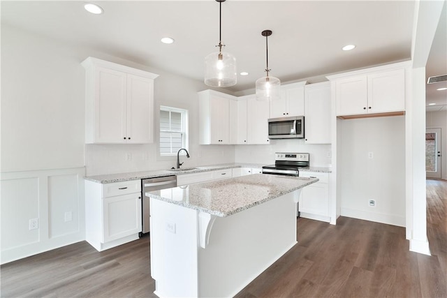 kitchen with white cabinets, appliances with stainless steel finishes, dark wood-type flooring, a center island, and a sink