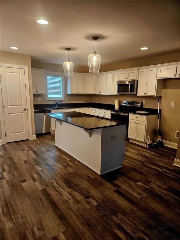 kitchen featuring appliances with stainless steel finishes, a center island, white cabinetry, a kitchen breakfast bar, and hanging light fixtures