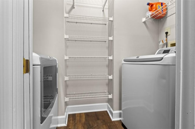 clothes washing area featuring laundry area, washing machine and dryer, baseboards, and dark wood finished floors