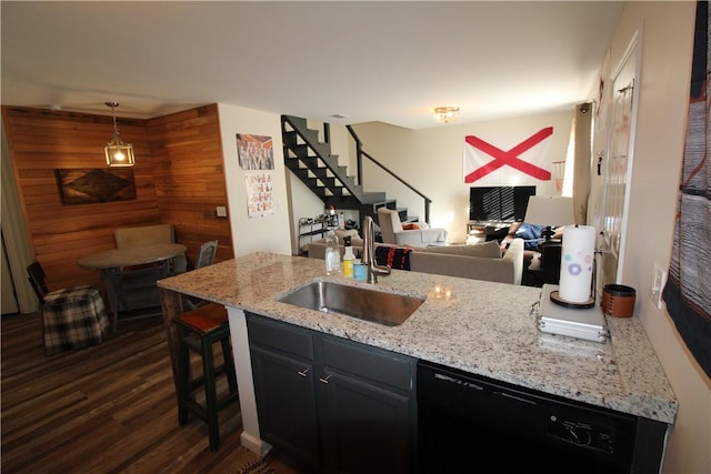 kitchen featuring dark wood-type flooring, sink, dishwasher, hanging light fixtures, and wood walls